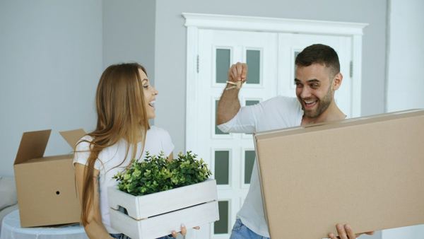 Two people carrying moving boxes into a new home